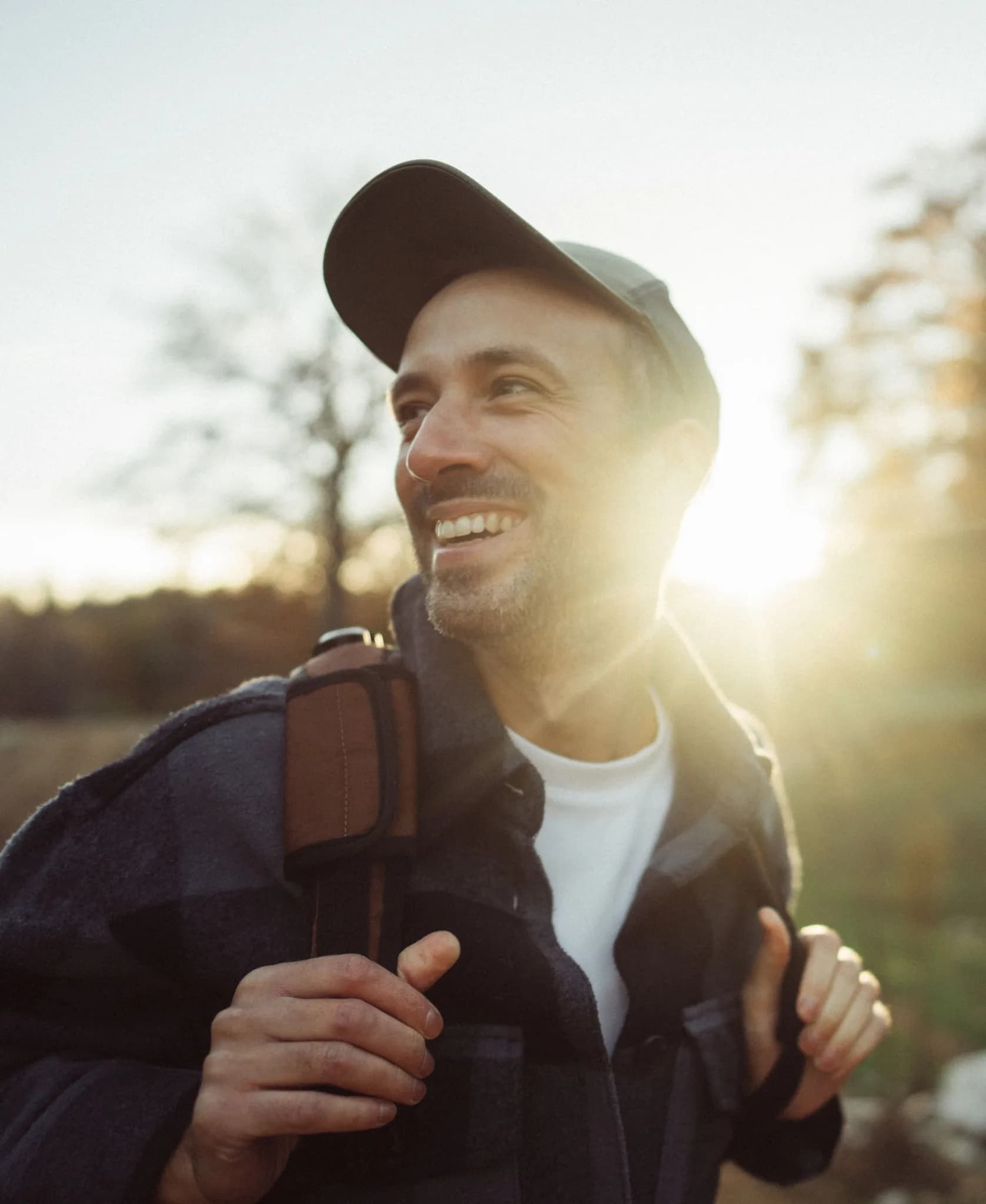 Uomo sorridente con zaino all'aperto nella luce della sera